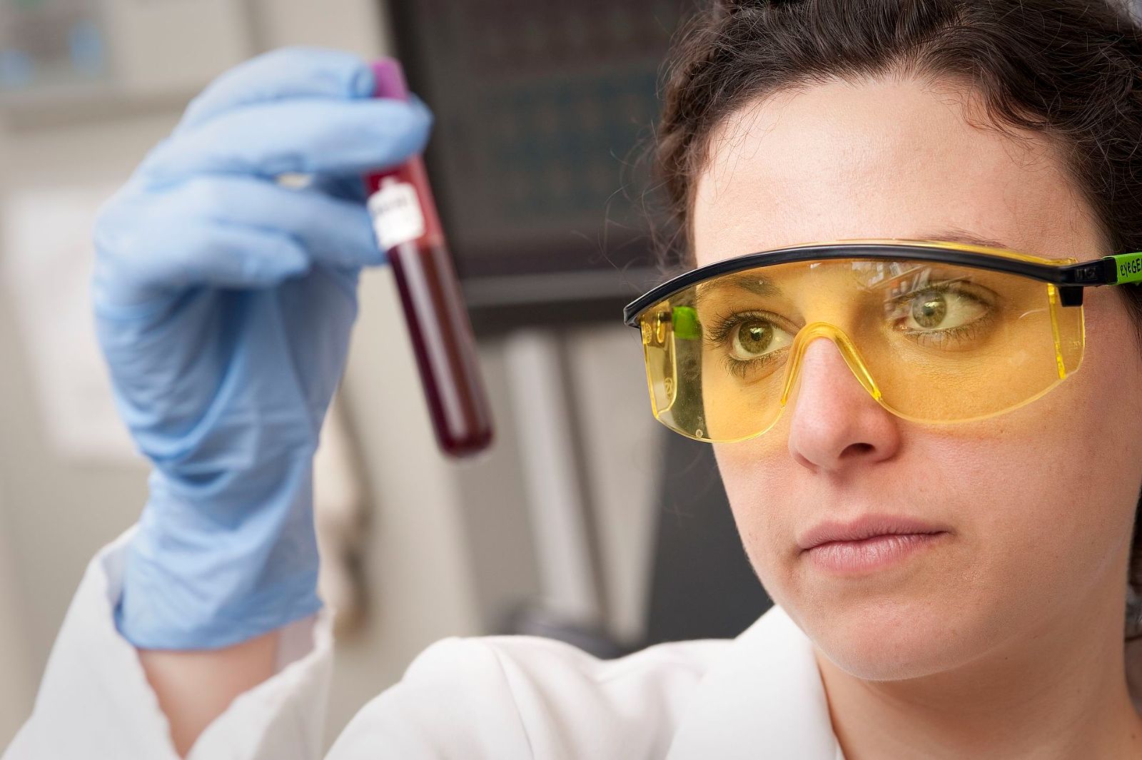 A lab technician in safety glasses checking a blood sample tube